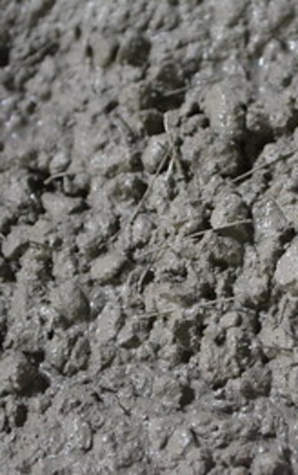 Nahaufnahme einer grobkörnigen, feuchten Betonoberfläche mit sichtbaren kurzen Fasern. Die Fasern bestehen aus Stahl und Kunststoff und sind unregelmäßig im Beton verteilt. Die Oberfläche wirkt rau, leicht glänzend und zeigt die typische Struktur von Faserbeton, der durch die Fasern zusätzliche Stabilität erhält.

                                    